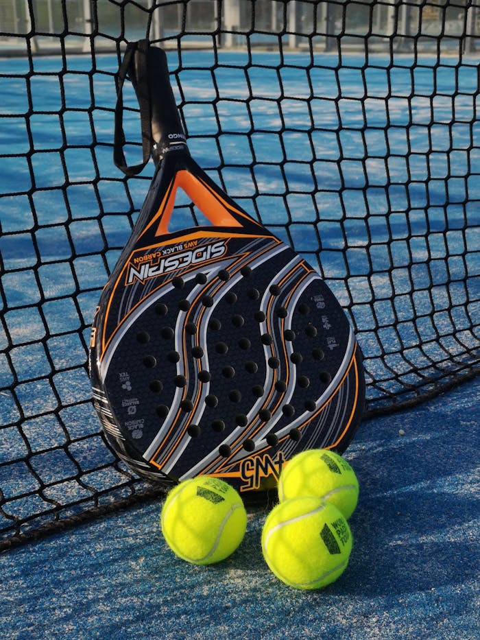 From above of padel racket and small colorful balls near fence on sports ground